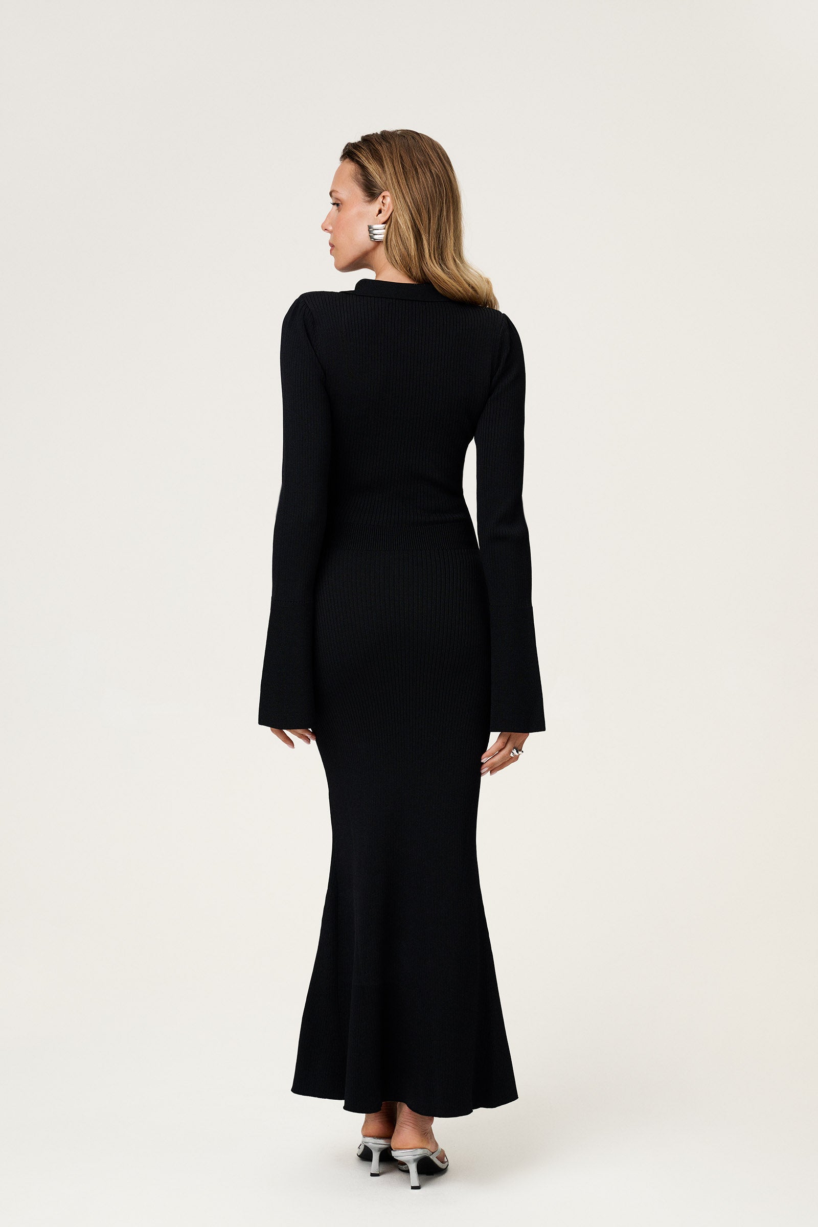 Woman wearing the knitted Basel maxi dress in black, featuring a cutout design at chest area and long, flared sleeves. image