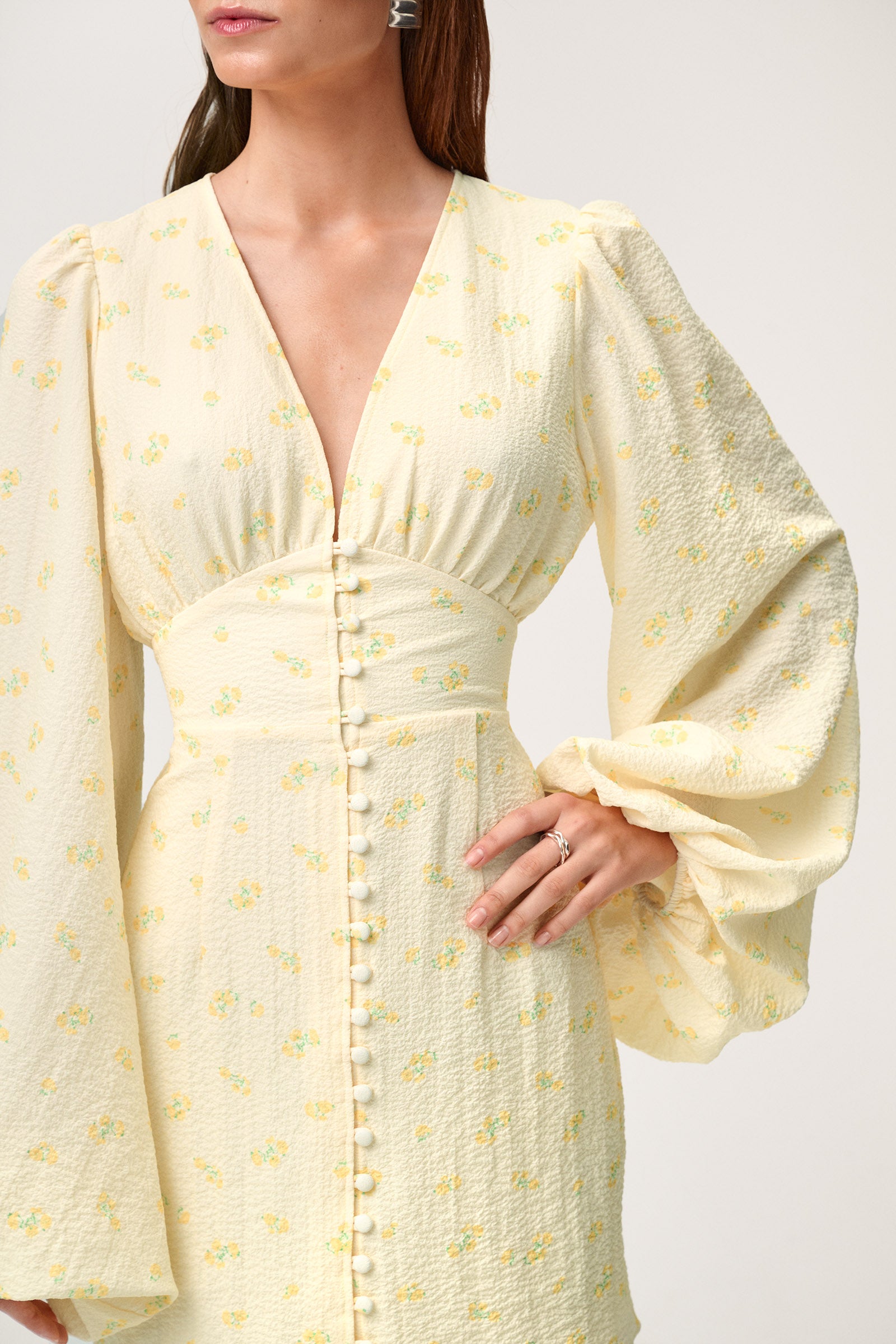 A model wearing a pastel yellow mini dress with wide balloon sleeves, a V-shaped neckline, and buttons along the front. The dress has a hidden zipper in the back and is fully lined.
 image