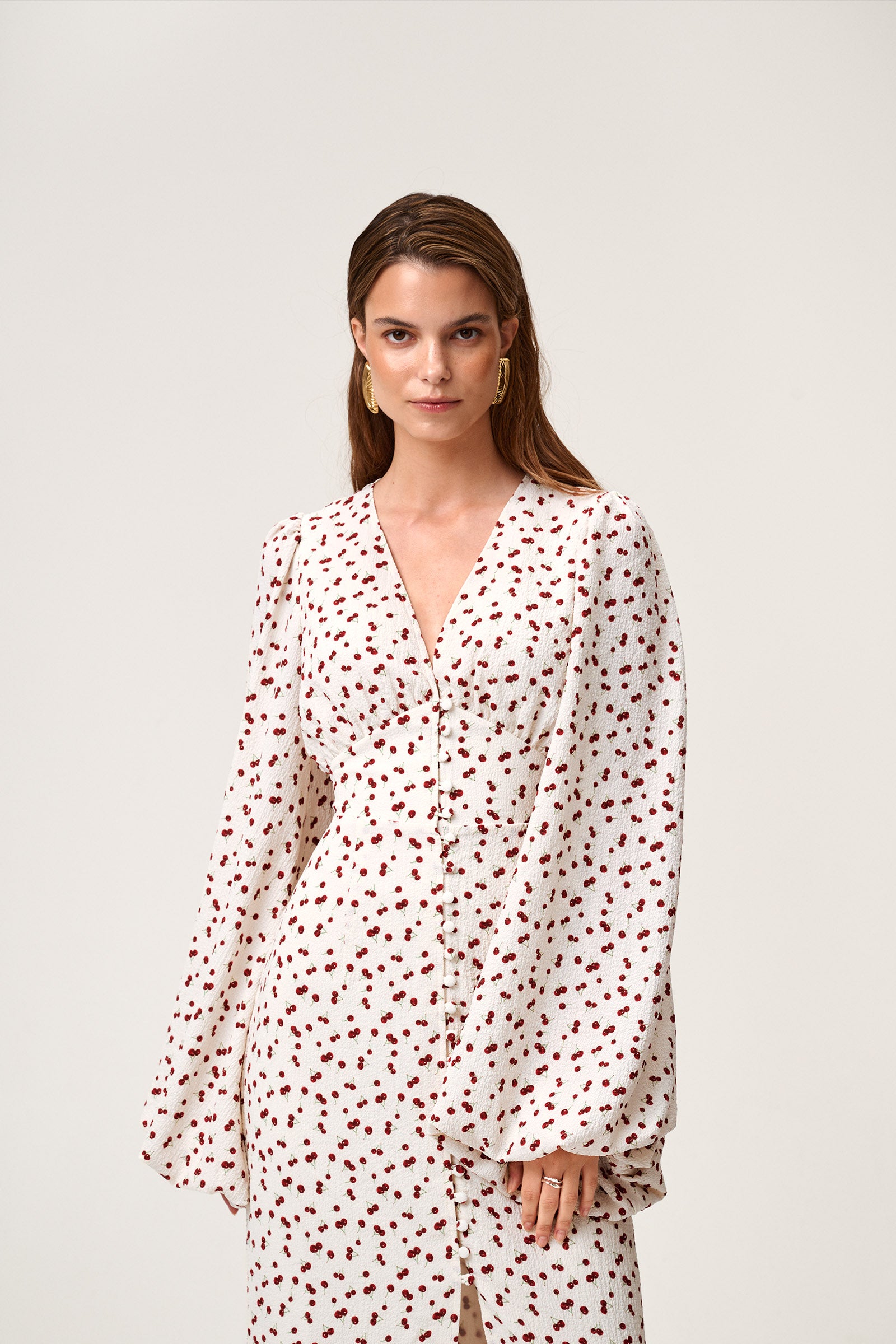 A model wearing Positano dress, size 34, a red cherry print maxi dress with long sleeves, a V-neck collar, and front slits. image