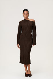 Woman wearing the Arona knitted midi dress in brown melange with one padded shoulder, full-length sleeves, a back slit, and a heavy cable-knit design. thumbnail image