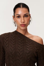 Woman wearing the Arona knitted midi dress in brown melange with one padded shoulder, full-length sleeves, a back slit, and a heavy cable-knit design.Woman wearing the Arona knitted midi dress in brown melange with one padded shoulder, full-length sleeves, a back slit, and a heavy cable-knit design. thumbnail image