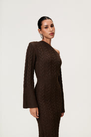 Woman wearing the Arona knitted midi dress in brown melange with one padded shoulder, full-length sleeves, a back slit, and a heavy cable-knit design. thumbnail image