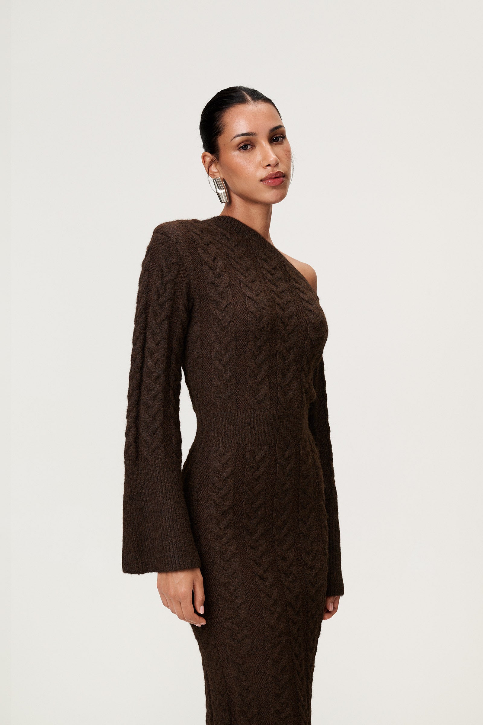 Woman wearing the Arona knitted midi dress in brown melange with one padded shoulder, full-length sleeves, a back slit, and a heavy cable-knit design. image