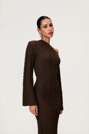 Woman wearing the Arona knitted midi dress in brown melange with one padded shoulder, full-length sleeves, a back slit, and a heavy cable-knit design. thumbnail image