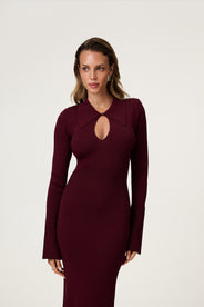 Woman wearing the Basel dress in burgundy, a knitted maxi with a collared cut-out neckline, decorative seams, and a flared hem. Finished with long sleeves and wide cuffs. thumbnail image