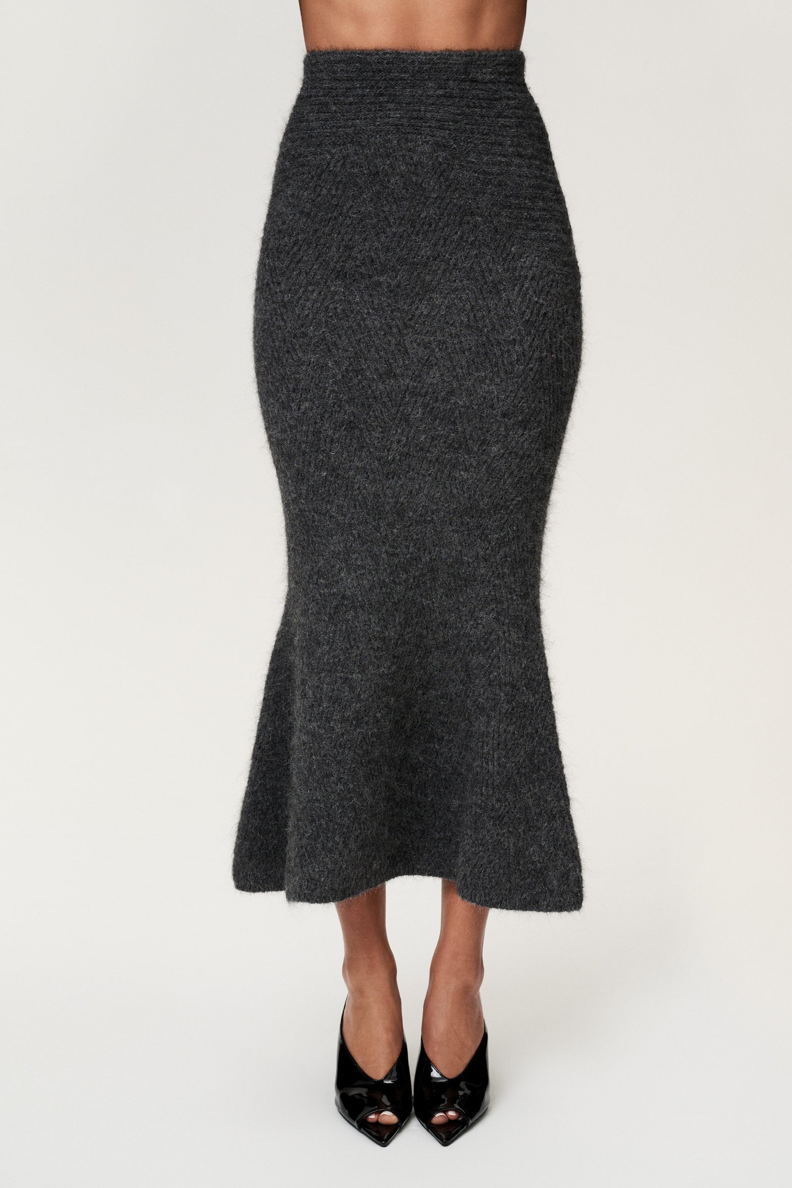 Woman wearing a Cessole midi skirt in dark grey. The skirt features a structured knit, midi length, zipper on the side, curved cutline in the waist, and softly flared bottom. image