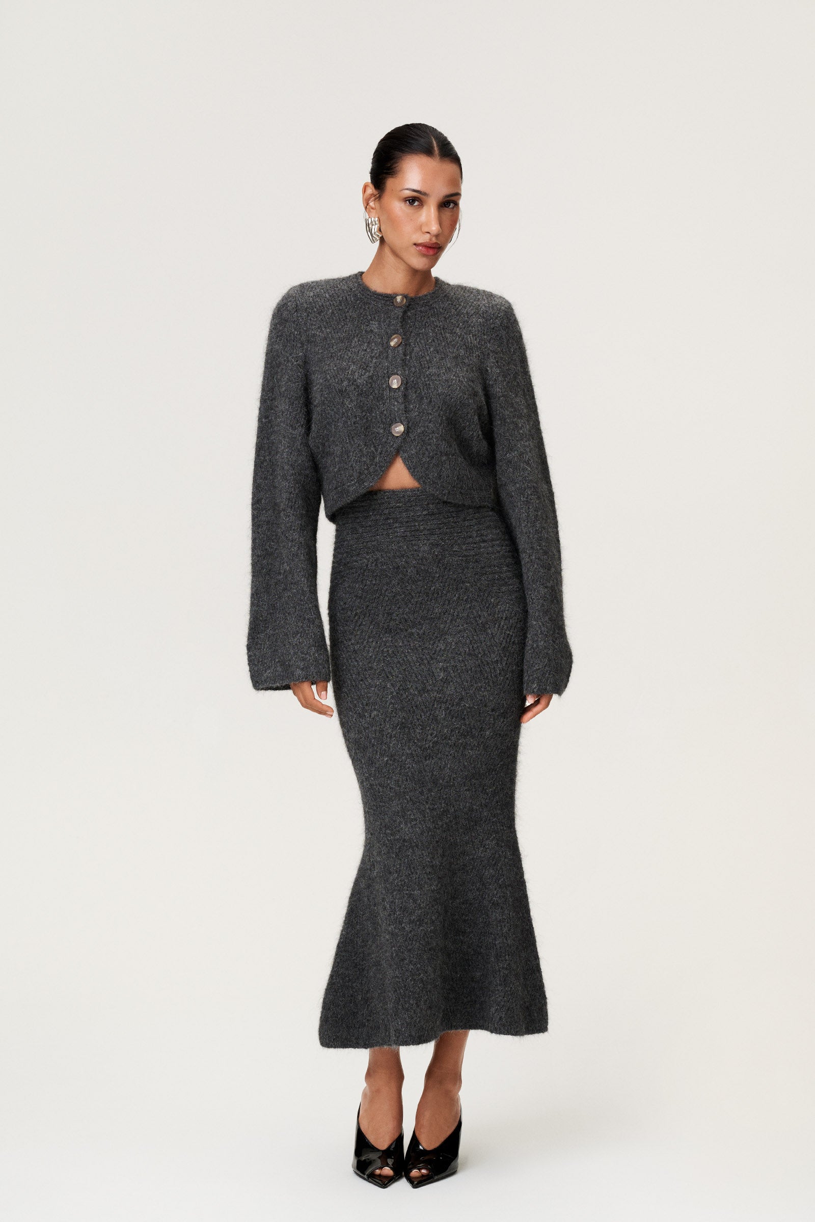 Woman wearing a Cessole midi skirt and Cessole cardigan in dark grey. The skirt features a structured knit, midi length, zipper on the side, curved cutline in the waist, and softly flared bottom. image