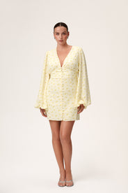A model wearing a pastel yellow mini dress with wide balloon sleeves, a V-shaped neckline, and buttons along the front. The dress has a hidden zipper in the back and is fully lined. thumbnail image