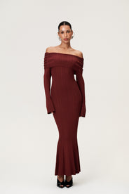 Woman wearing the Izano dress in burgundy, a knitted off-shoulder maxi dress with ruched panel detailing, soft draping, and a flowing, cozy silhouette. thumbnail image