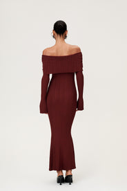 Woman wearing the Izano dress in burgundy, a knitted off-shoulder maxi dress with ruched panel detailing, soft draping, and a flowing, cozy silhouette. thumbnail image