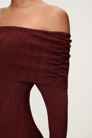 Woman wearing the Izano dress in burgundy, a knitted off-shoulder maxi dress with ruched panel detailing, soft draping, and a flowing, cozy silhouette. thumbnail image