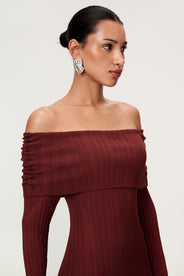 Woman wearing the Izano dress in burgundy, a knitted off-shoulder maxi dress with ruched panel detailing, soft draping, and a flowing, cozy silhouette. thumbnail image