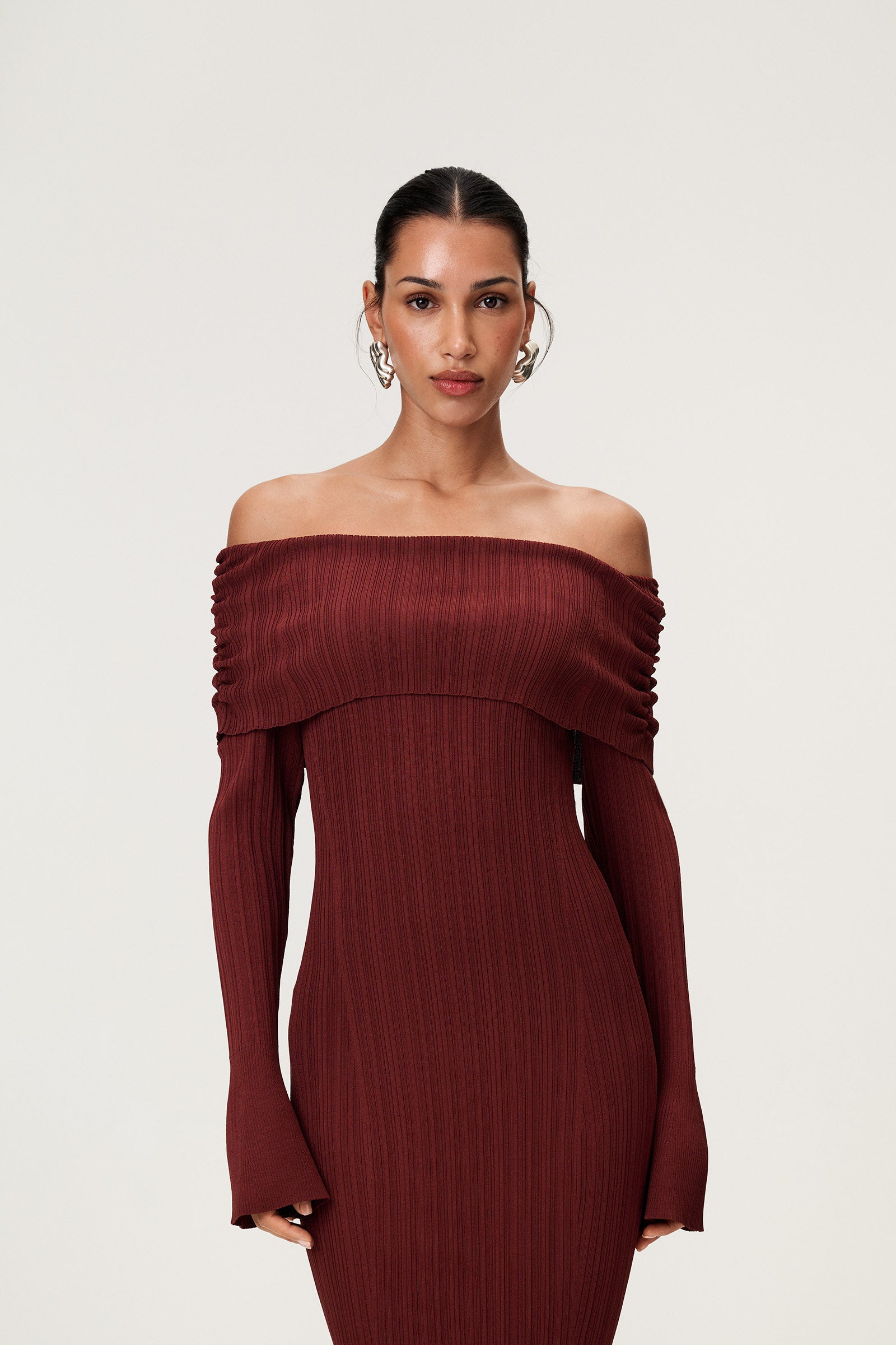 Woman wearing the Izano dress in burgundy, a knitted off-shoulder maxi dress with ruched panel detailing, soft draping, and a flowing, cozy silhouette. image