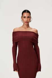 Woman wearing the Izano dress in burgundy, a knitted off-shoulder maxi dress with ruched panel detailing, soft draping, and a flowing, cozy silhouette. thumbnail image