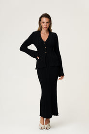 Woman wearing Lugo Cardigan, size 36, a black knitted cardigan, low front with brown buttons and long sleeves.  thumbnail image