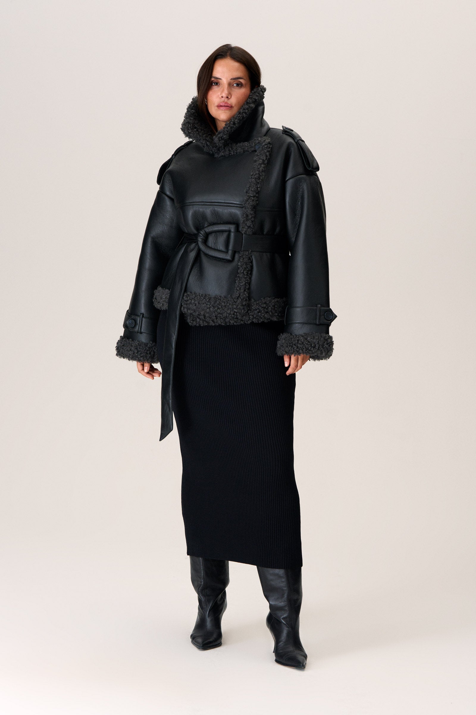 A model wearing a black Manchester cropped jacket with oversized fit, faux shearling lining, side pockets, and a belt with a D-shaped buckle. image