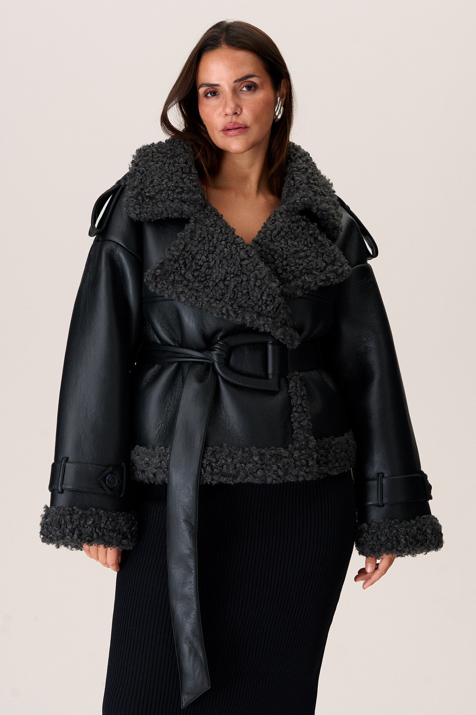 A model wearing a black Manchester cropped jacket with oversized fit, faux shearling lining, side pockets, and a belt with a D-shaped buckle. image