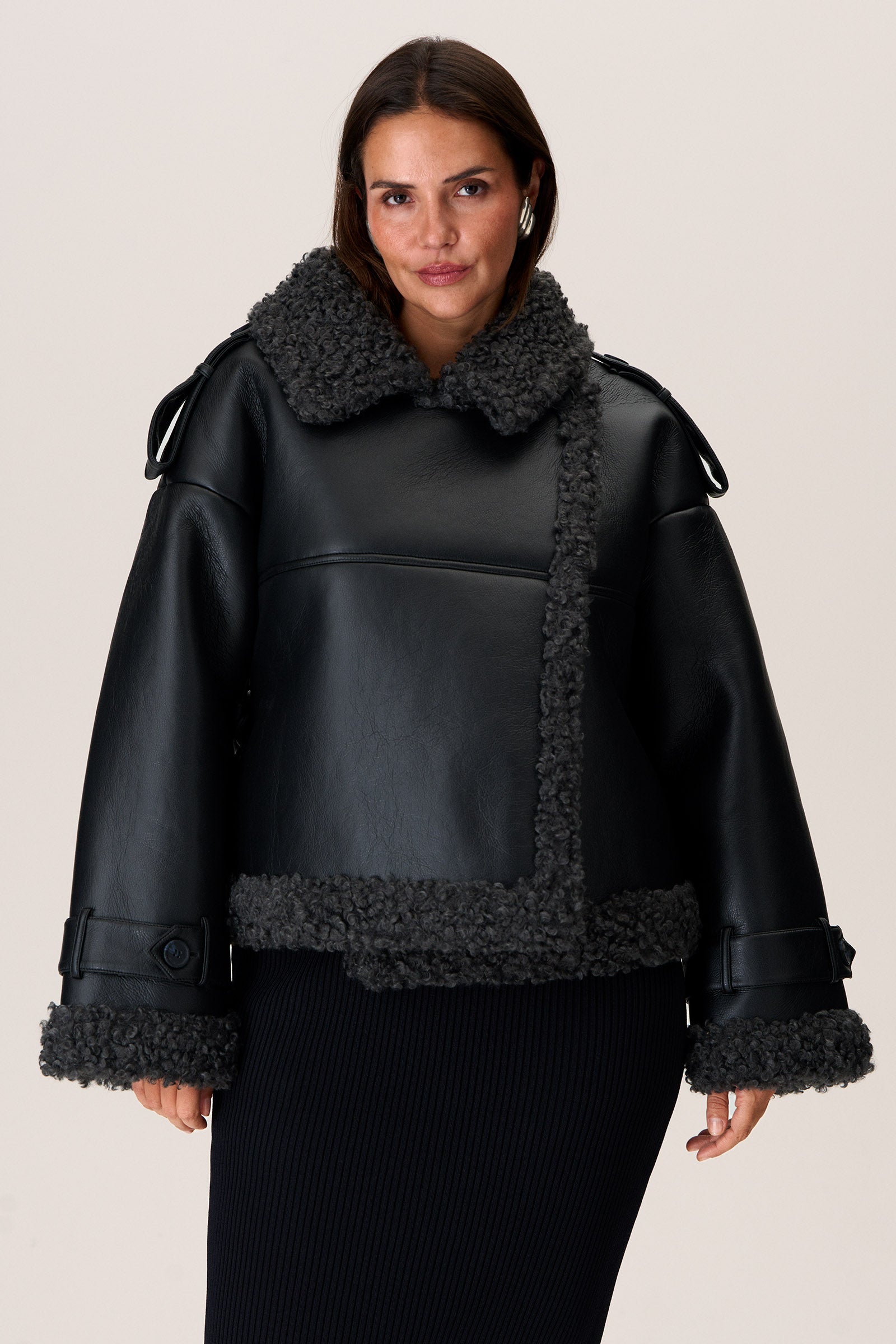 A model wearing a black Manchester cropped jacket with oversized fit, faux shearling lining, side pockets, and a belt with a D-shaped buckle. image