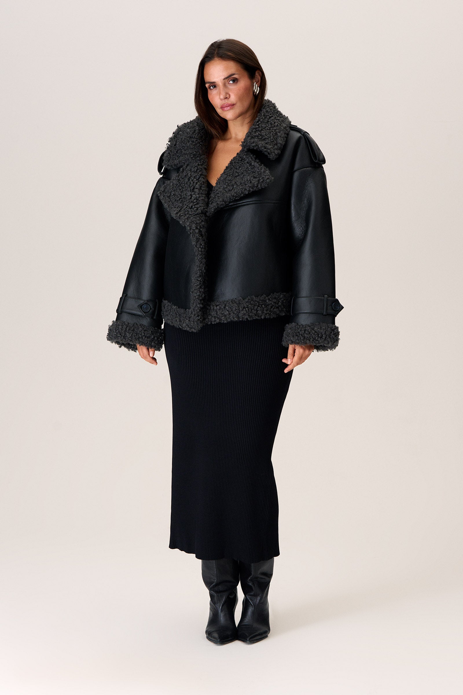 A model wearing a black Manchester cropped jacket with oversized fit, faux shearling lining, side pockets, and a belt with a D-shaped buckle. image