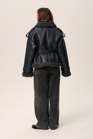 A model wearing a black Manchester cropped jacket with oversized fit, faux shearling lining, side pockets, and a belt with a D-shaped buckle. thumbnail image