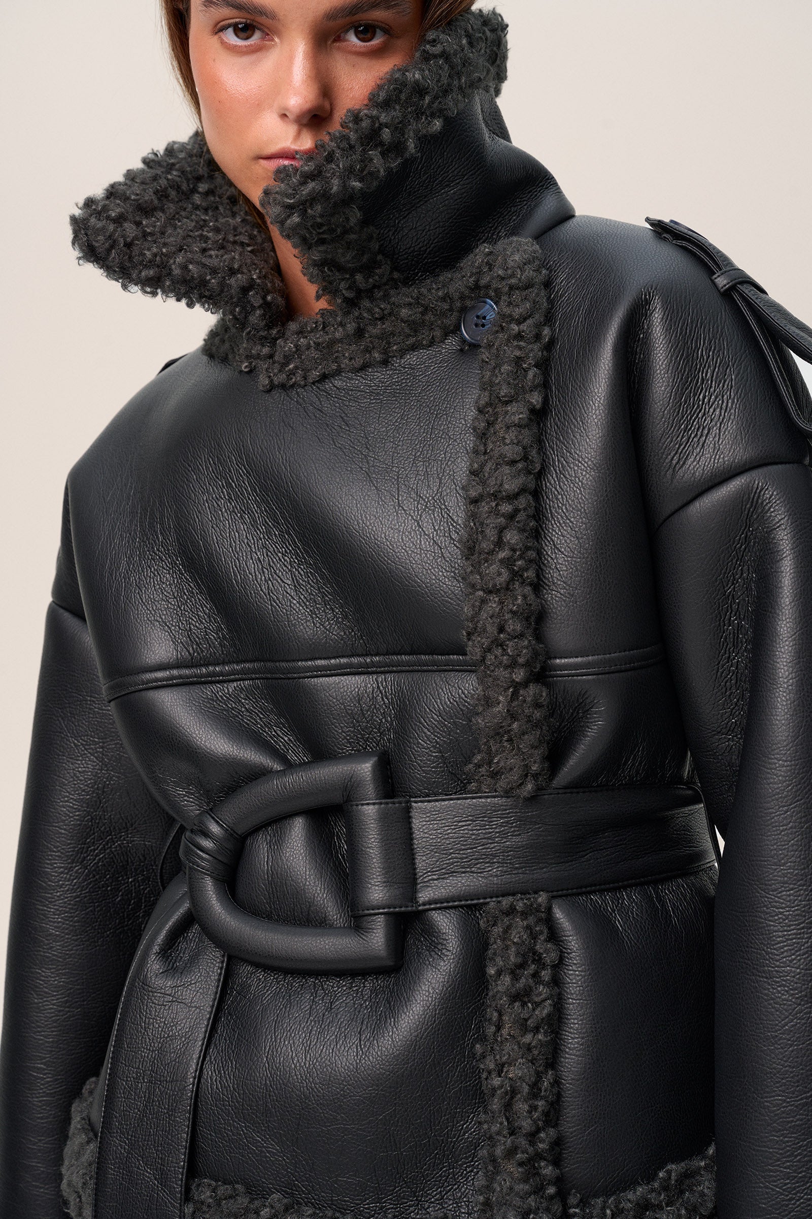 A model wearing a black Manchester cropped jacket with oversized fit, faux shearling lining, side pockets, and a belt with a D-shaped buckle. image