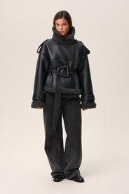 A model wearing a black Manchester cropped jacket with oversized fit, faux shearling lining, side pockets, and a belt with a D-shaped buckle. thumbnail image