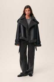 A model wearing a black Manchester cropped jacket with oversized fit, faux shearling lining, side pockets, and a belt with a D-shaped buckle. thumbnail image