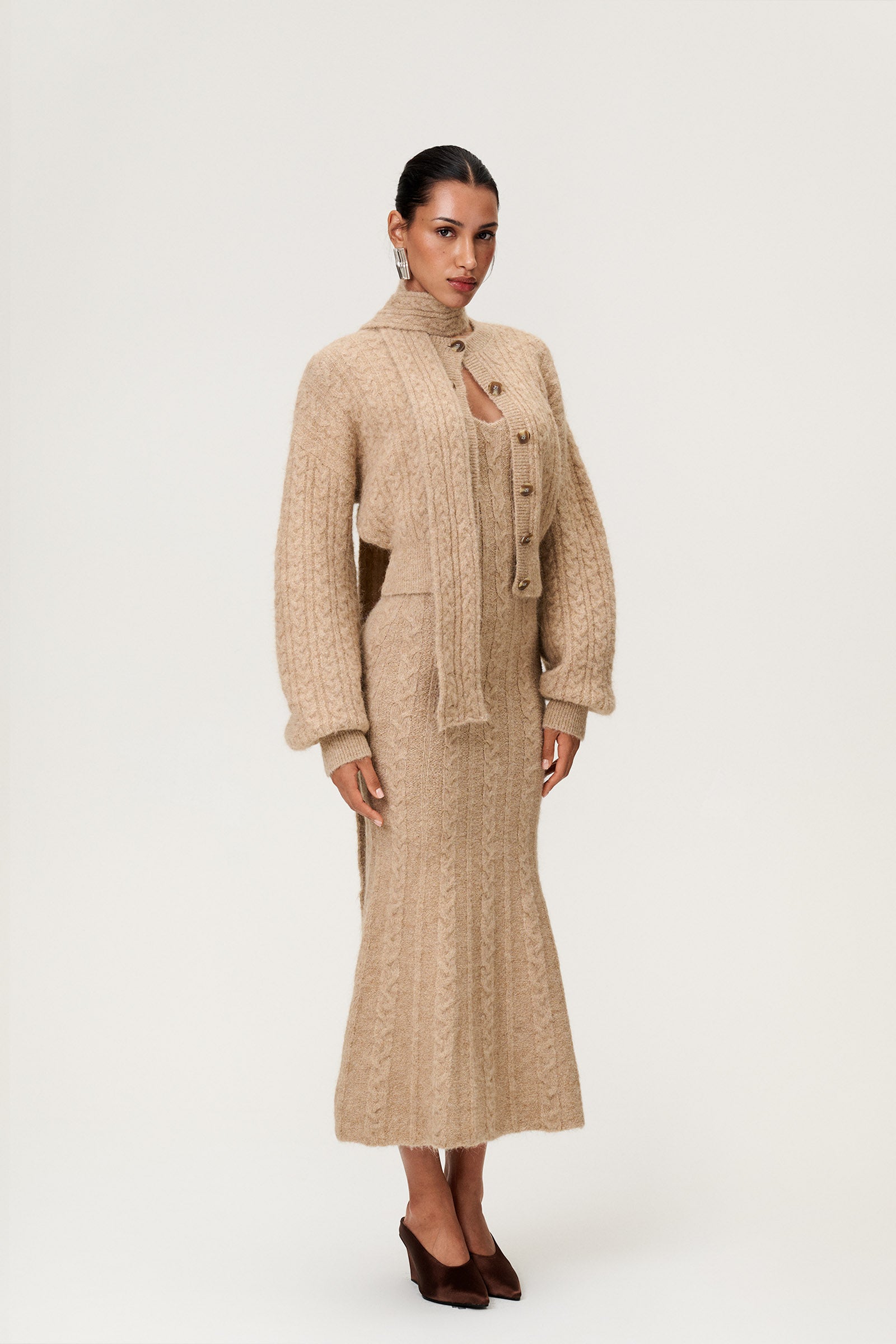 Woman wearing the Merano scarf and Merano cardigan styled with the Merano maxi dress in beige melange, a sleek, figure-flattering style with delicate singlet straps, a deep V-neckline, and an hourglass fit. image