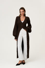 Woman wearing the Montana maxi dress in brown melange styled as a cardigan with jeans. The dress features an hourglass knit with a button-up front, V-neck collar, and balloon sleeves with cuff details. thumbnail image