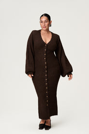 Woman wearing a brown knitted dress with button details, and ballon sleves on a white background. Styled with black low heels.  thumbnail image
