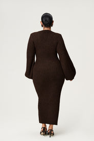 Image from the back. Woman wearing a brown knitted dress with button details, and ballon sleeves on a white background. Styled with black low heels.  thumbnail image