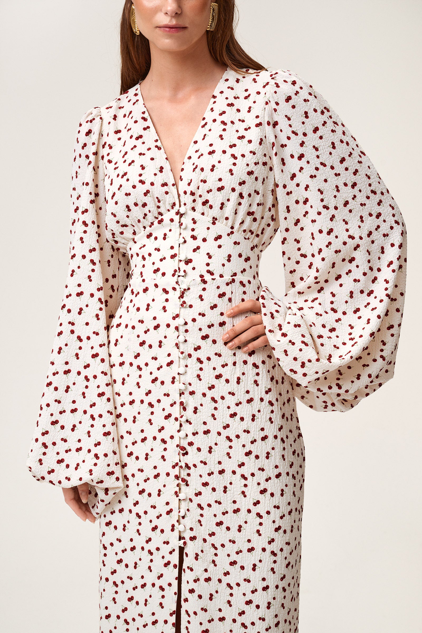 A model wearing Positano dress, size 34, a red cherry print maxi dress with long sleeves, a V-neck collar, and front slits. image