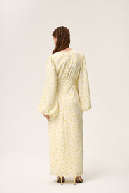 Image from the back. A woman wearing a pastel yellow maxi dress with long sleeves and a hidden zipper at the back. thumbnail image