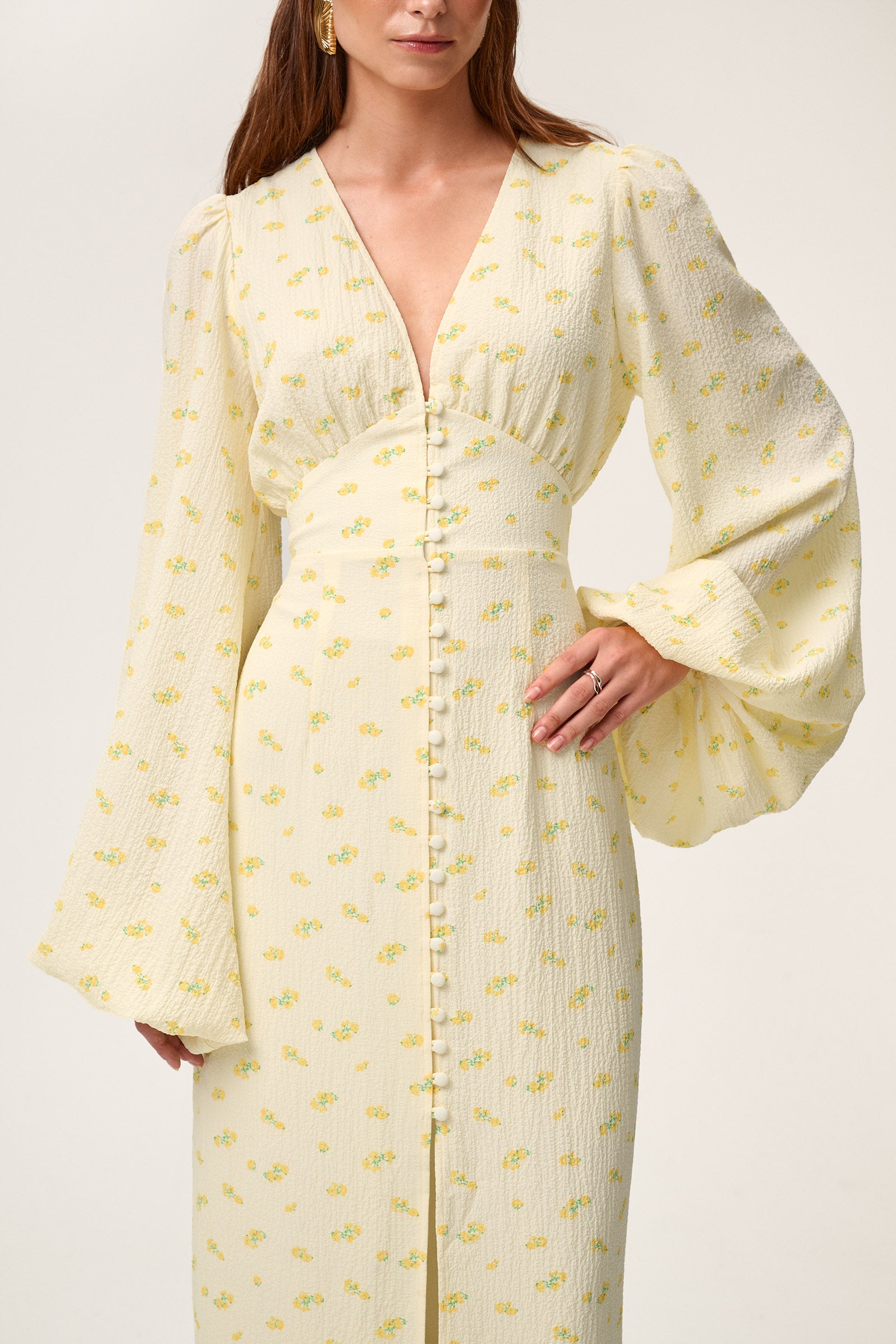 A woman wearing Positano dress, a pastel yellow maxi dress with long sleeves, a V-neck collar, buttons and slits at the front, and a hidden zipper at the back. image