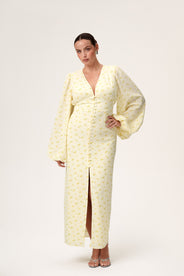 A woman wearing Positano dress, a pastel yellow maxi dress with long sleeves, a V-neck collar, buttons and slits at the front, and a hidden zipper at the back. thumbnail image