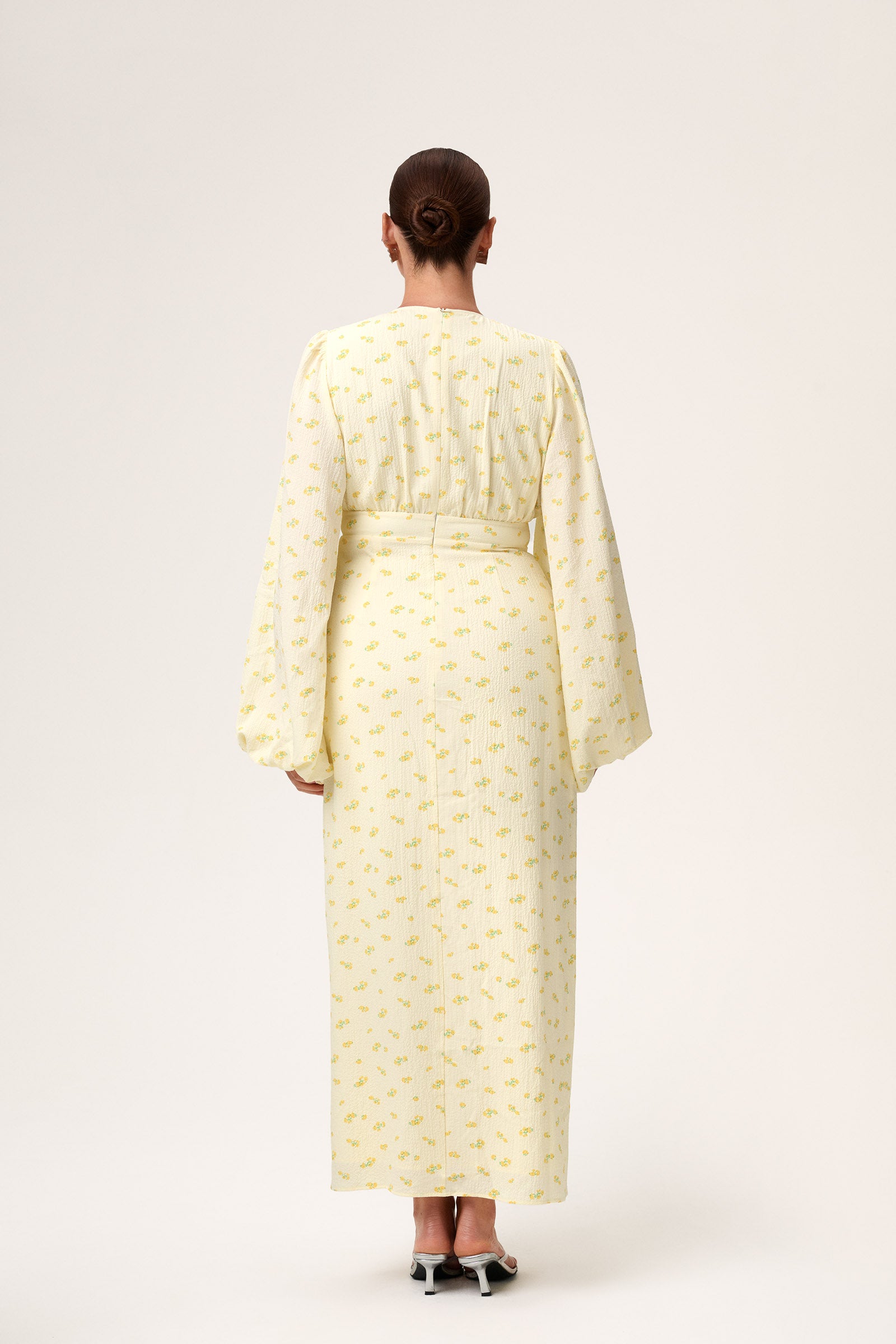 A woman wearing Positano dress, a pastel yellow maxi dress with long sleeves, a V-neck collar, buttons and slits at the front, and a hidden zipper at the back. image