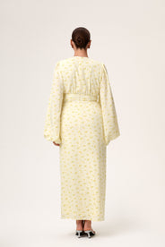 A woman wearing Positano dress, a pastel yellow maxi dress with long sleeves, a V-neck collar, buttons and slits at the front, and a hidden zipper at the back. thumbnail image