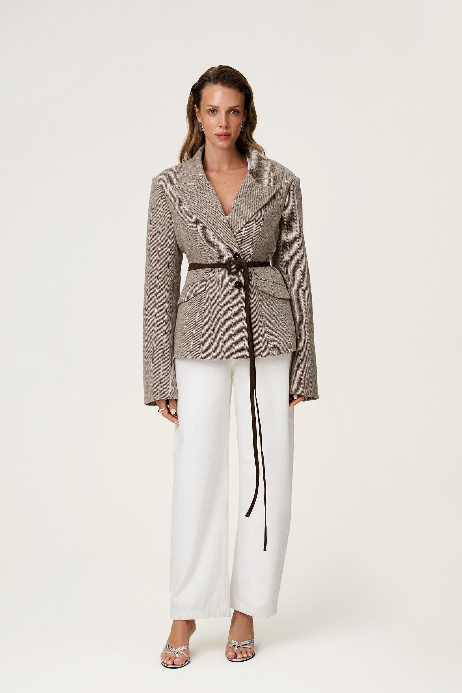 brown tweed blazer with buttons in the front and padded shoulders, fitted waist and long arms. fitted with white pants and brown suede belt in waist image