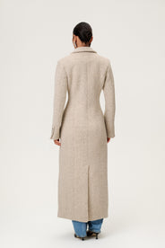 Woman wearing the Stockholm coat in beige melange. A full-length, hourglass coat with a cinched waist, removable suede belt, and structured shoulders. Finished with front pockets and a fully lined interior for warmth and comfort. thumbnail image
