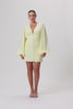 A model wearing a pastel yellow mini dress with wide balloon sleeves, a V-shaped neckline, and buttons along the front. The dress has a hidden zipper in the back and is fully lined.